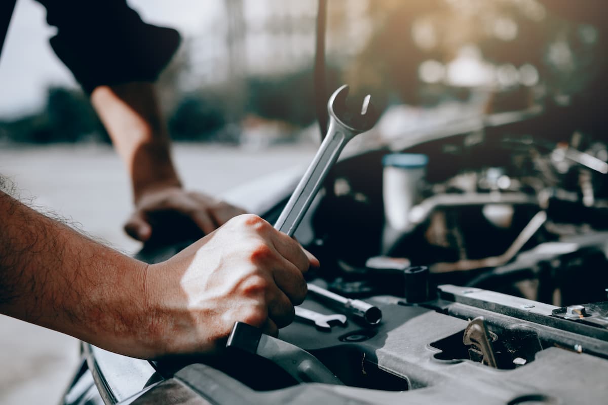 Un mécanicien tenant une clé, au dessus moteur d'une voiture