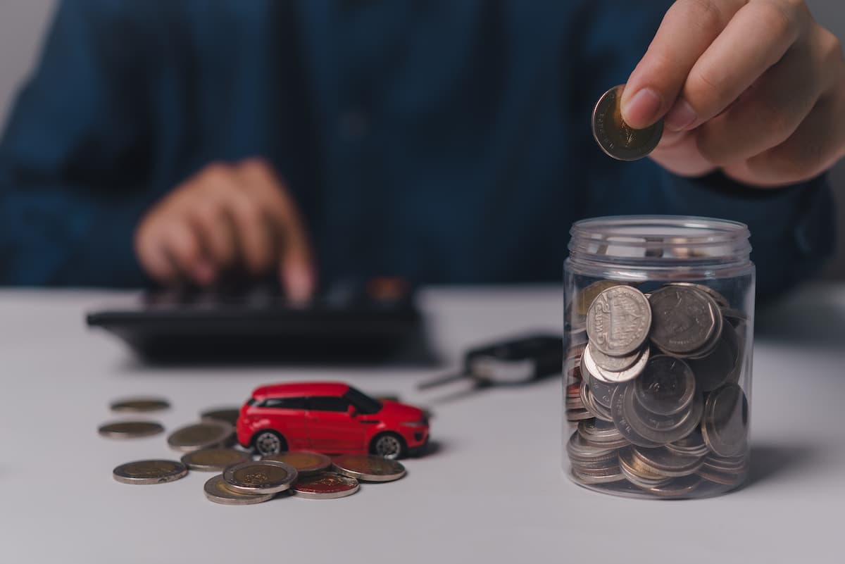 Personne calculant économies avec des pièces de monnaie, une petite voiture