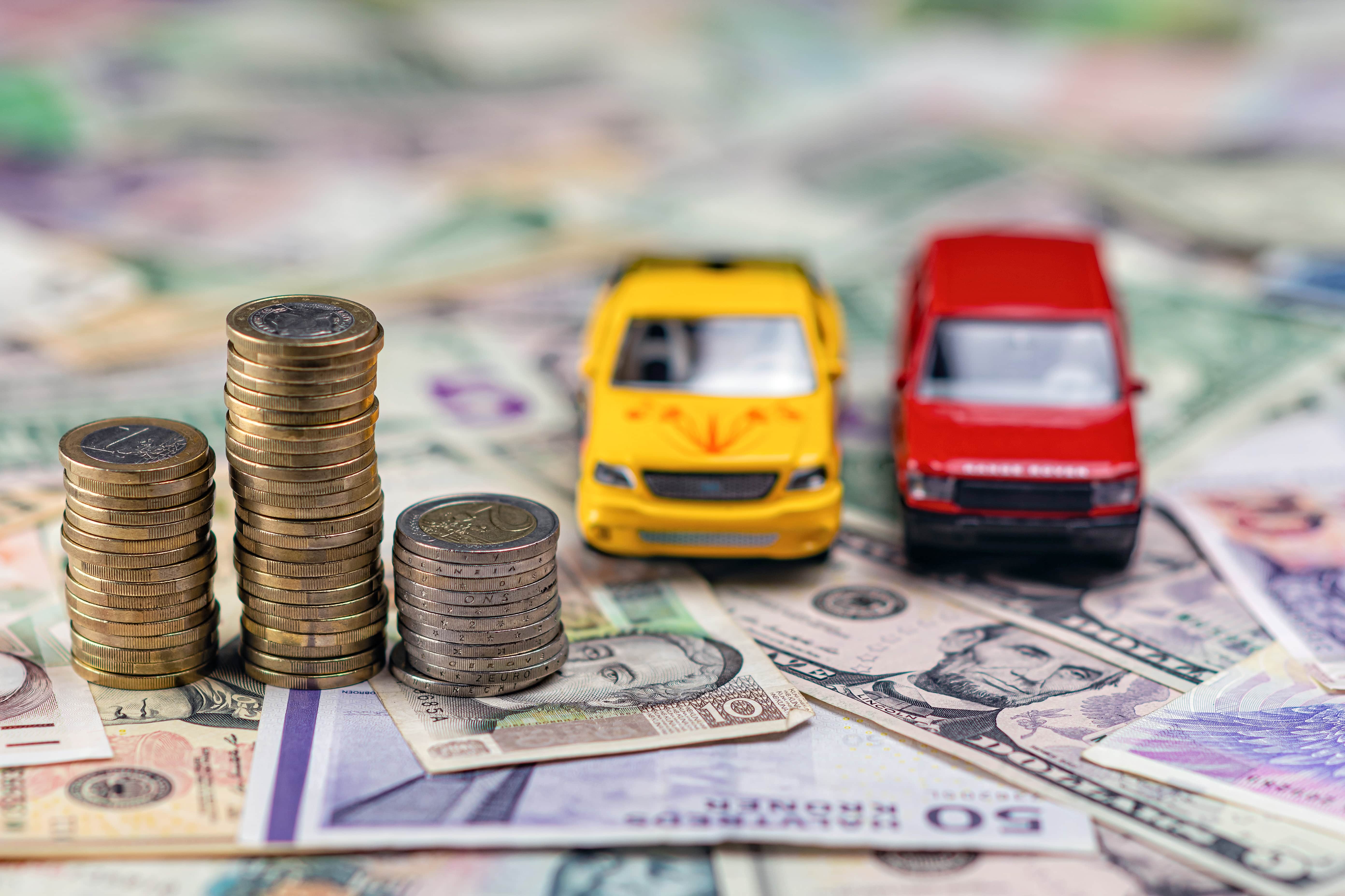 Pieces empilees devant des miniatures de voitures sur des billets
