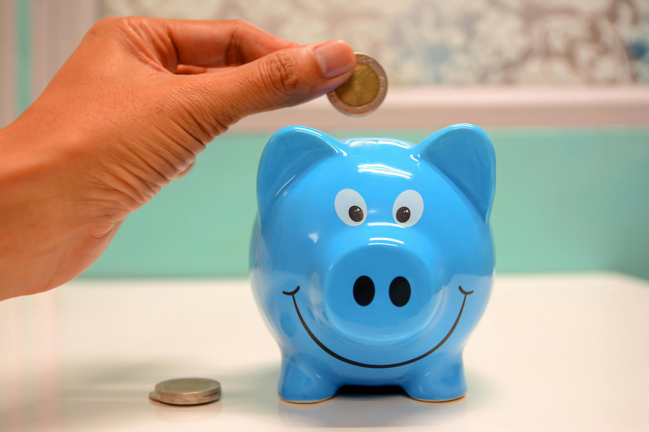 Main mettant une piece de monnaie dans une tirelire bleue en forme de cochon souriant