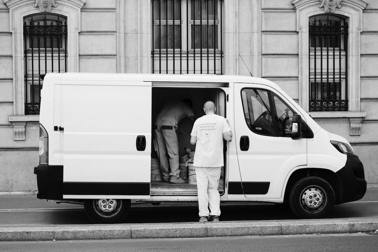 Artisans chargeant leur matériel dans un utilitaire d'occasion blanc garé en ville